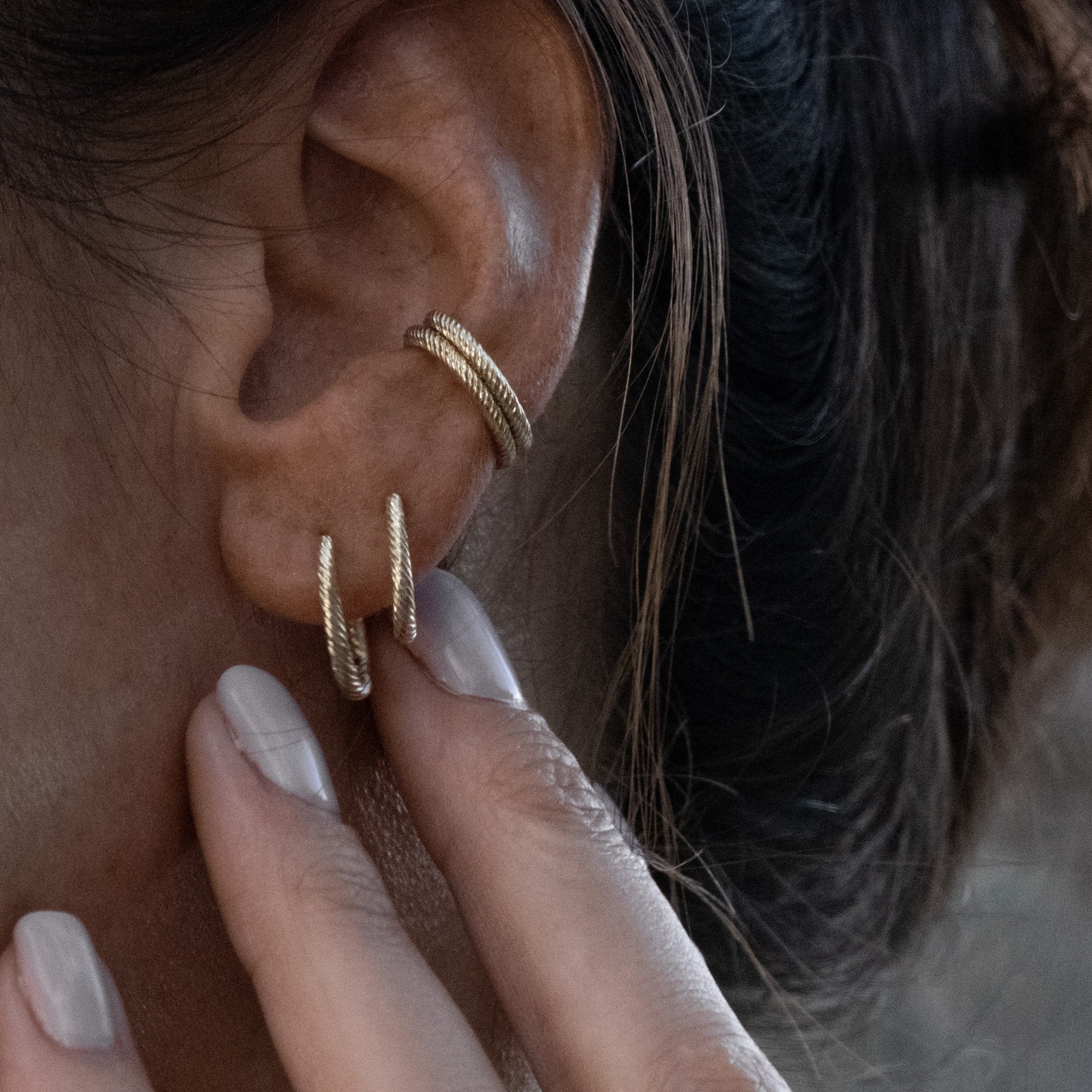 Solid gold hoop and huggie earrings styled with doubled ear cuffs featuring twisted texture, worn in a minimalist ear stack.
