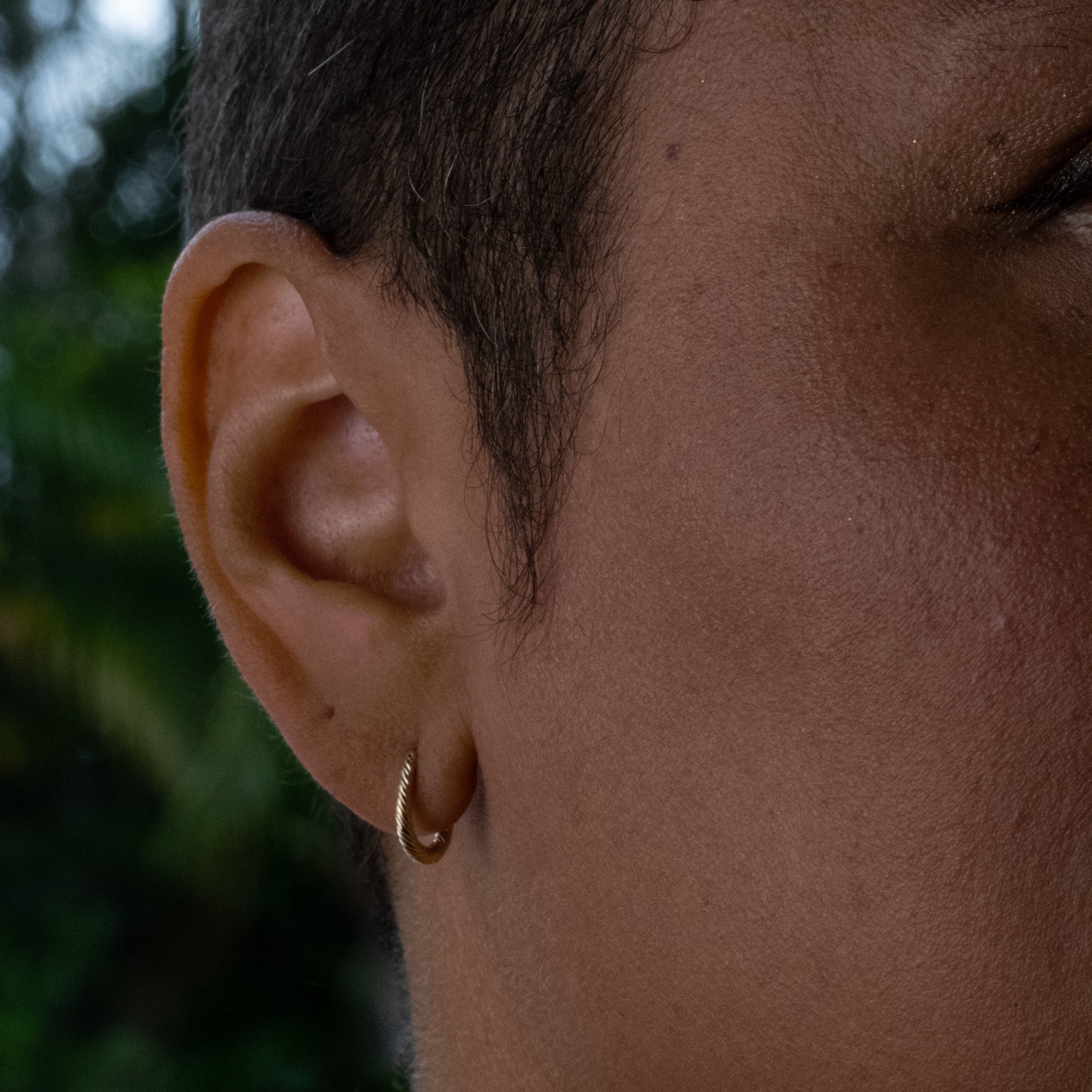 Angled view of solid gold huggie hoop earring with twisted texture and minimalist design, worn on ear.