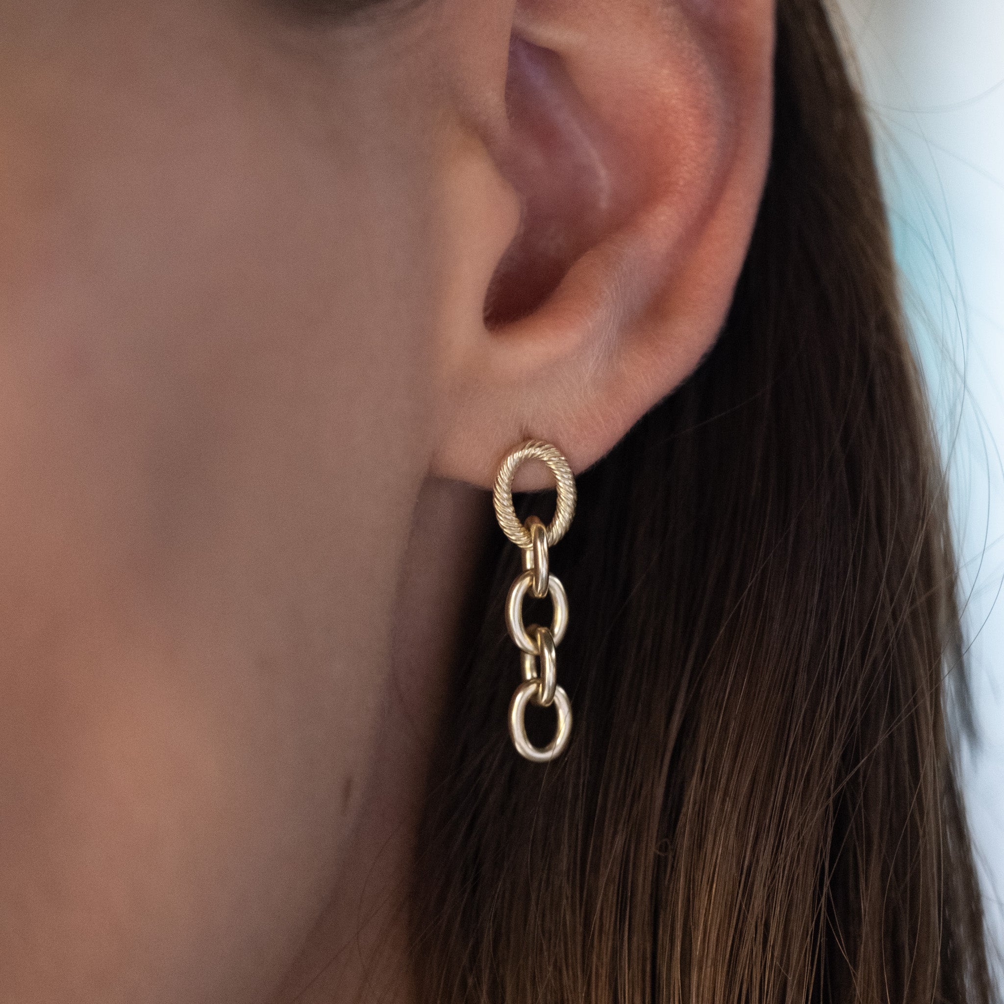 Long solid gold dangle earring with twisted texture and polished oval cable chain links, worn on ear.