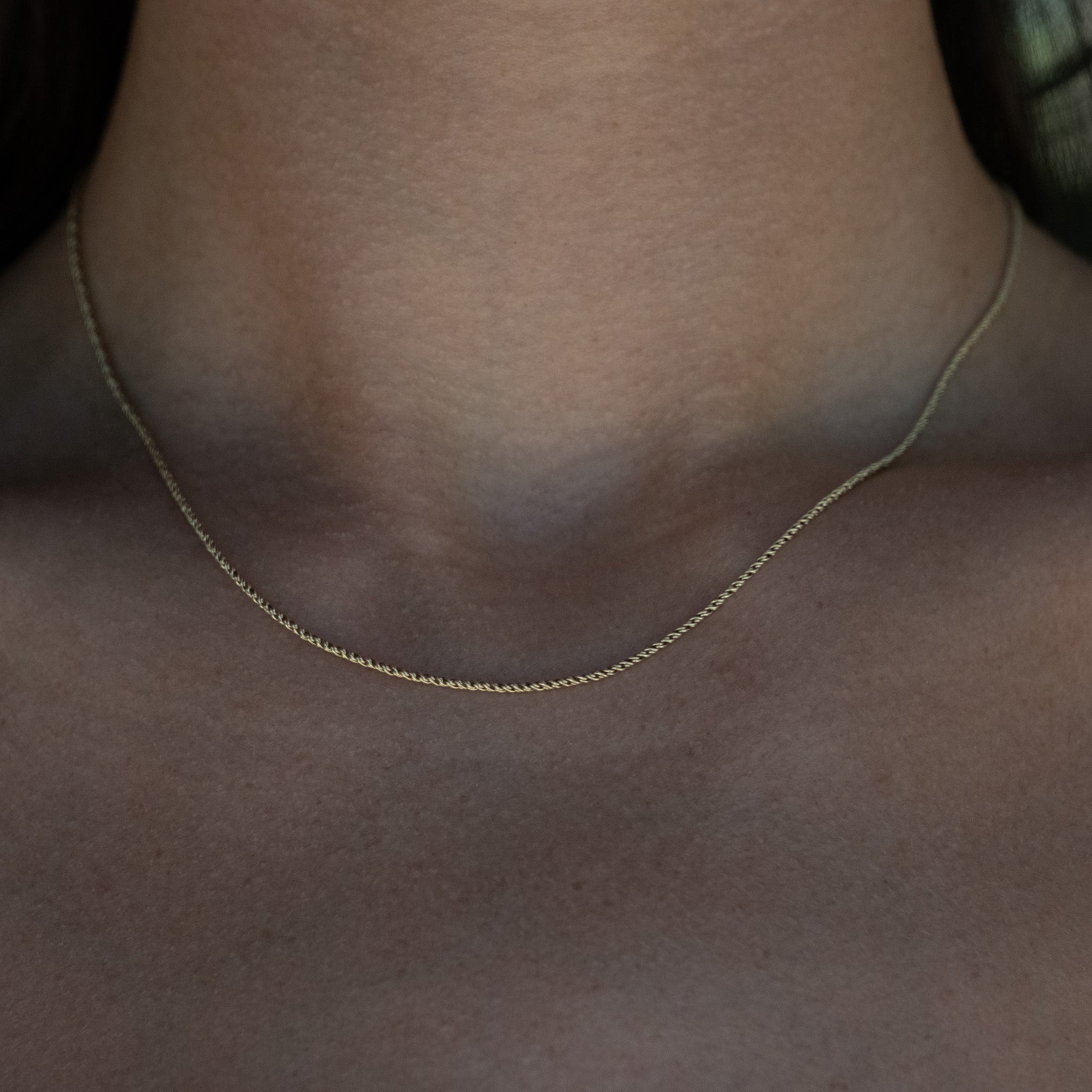 Solid gold rope chain necklace with tightly twisted links, worn on neck.