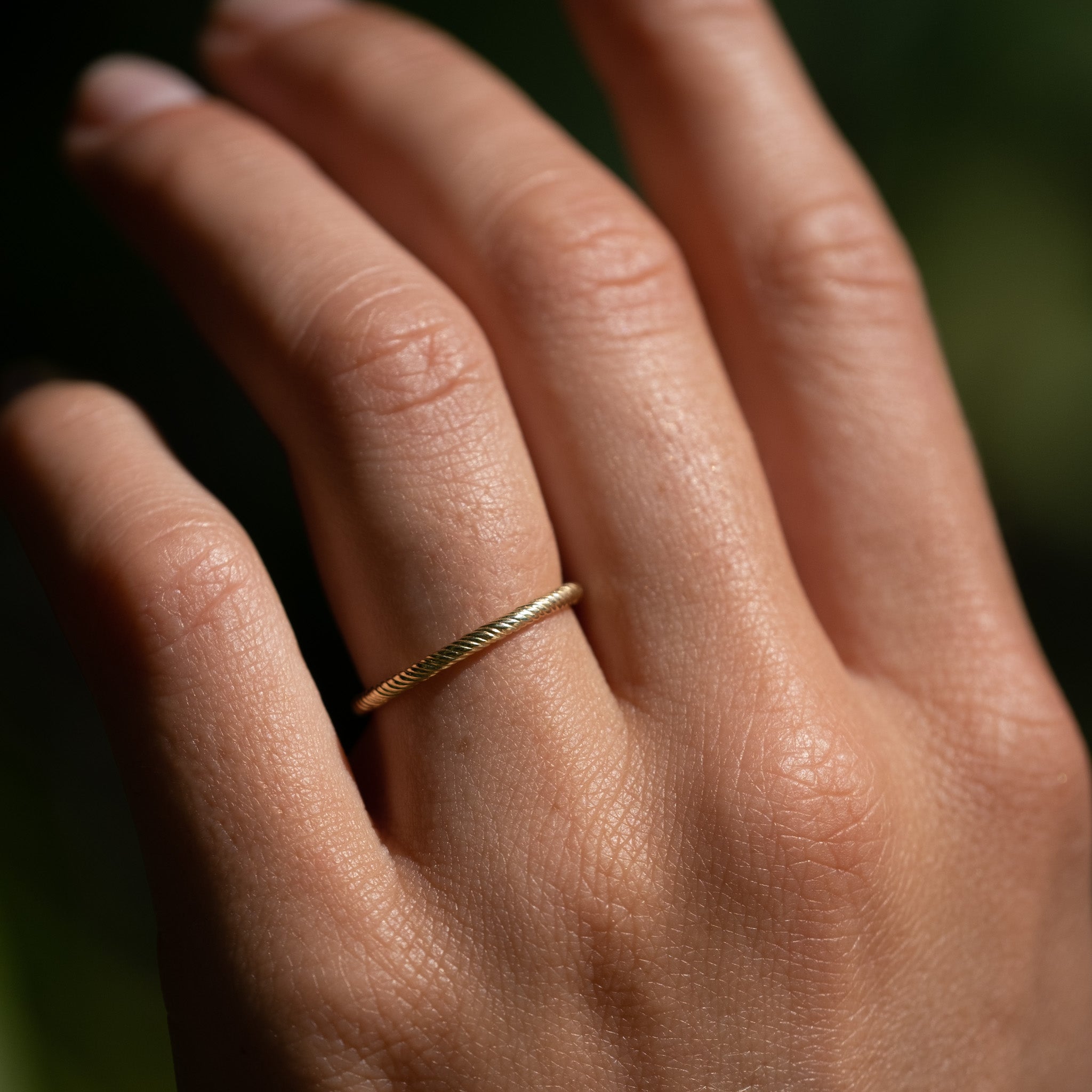 Solid gold stackable thin band ring with twisted texture and minimalist design, worn on hand.