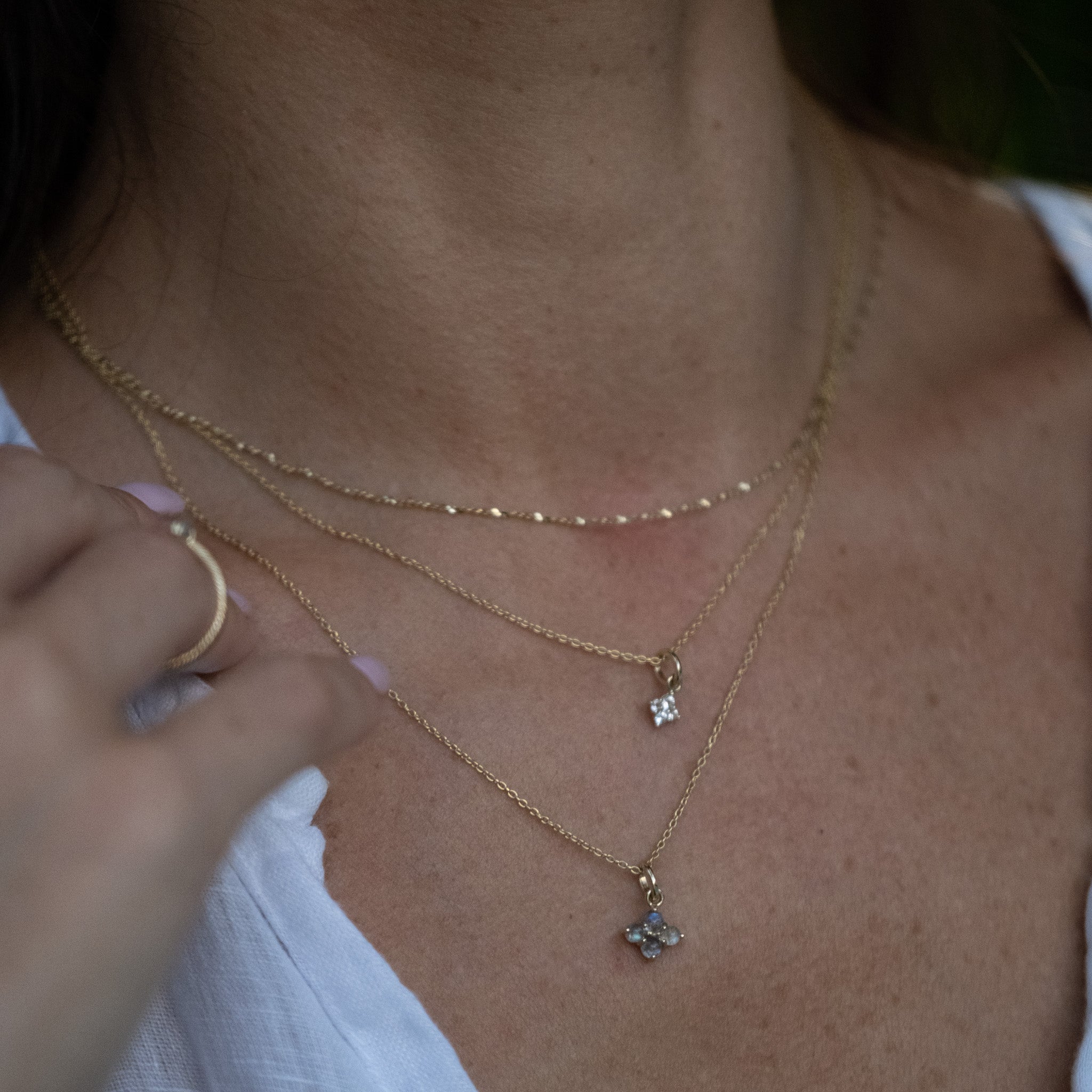 Shining solid gold charm pendants and chain necklaces featuring labradorite and white sapphire, layered on neck.