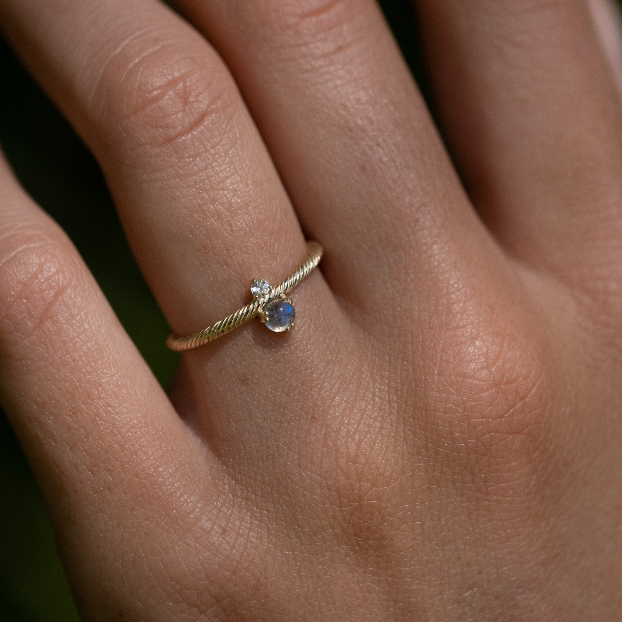 Solid gold ring with twisted texture, glowing labradorite, white sapphire, and minimalist design, worn on hand.