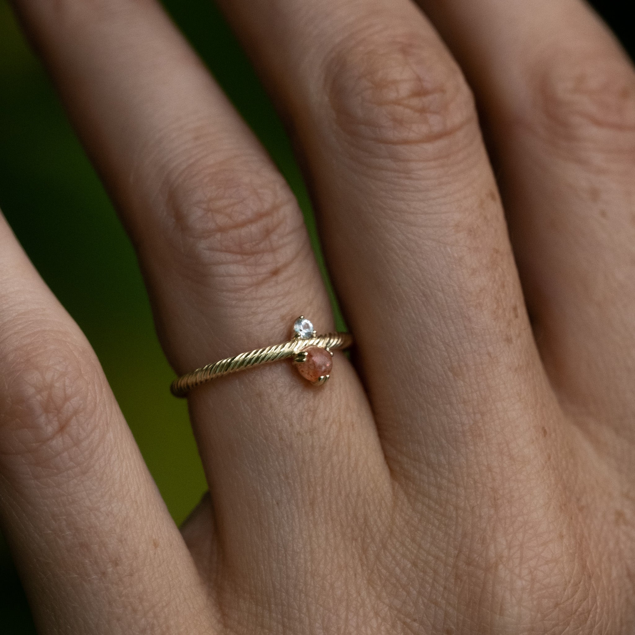 Solid gold ring with twisted texture, sunstone, white sapphire, and minimalist design, worn on hand.