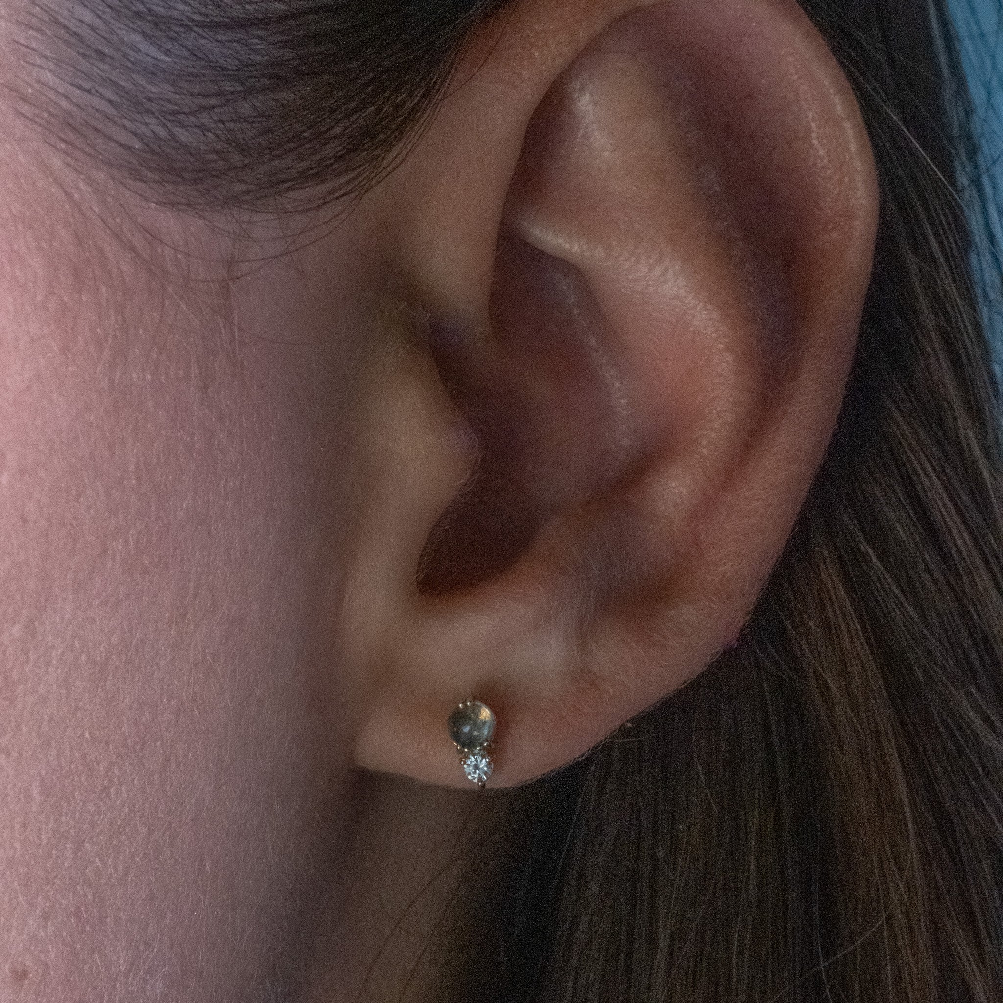 Solid gold stud earring with labradorite and white sapphire in a minimalist design, worn on ear.