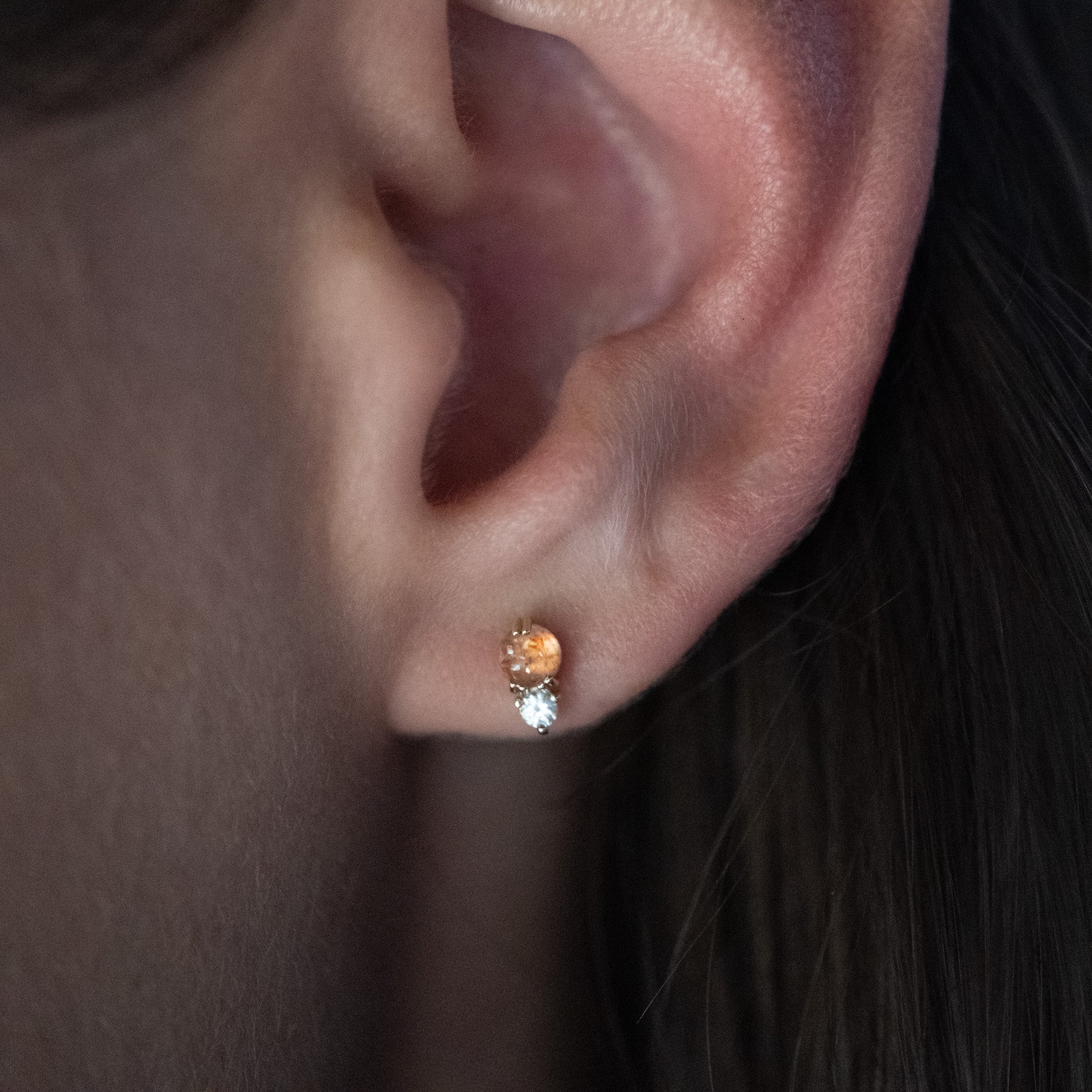 Solid gold stud earring with sunstone and white sapphire in a minimalist design, worn on ear.