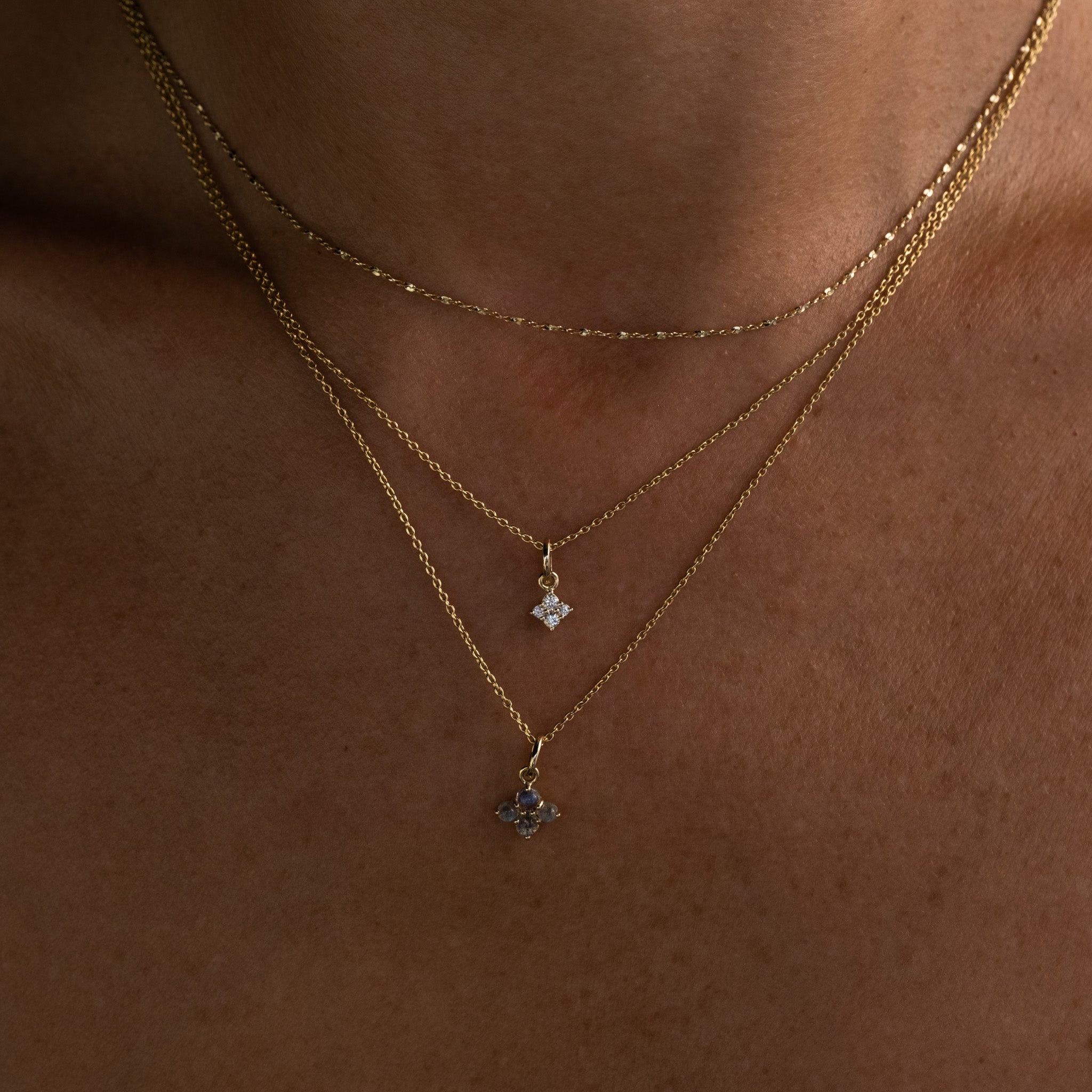Solid gold white sapphire and labradorite charm pendants in minimalist celestial designs on chain necklaces, layered on neck.