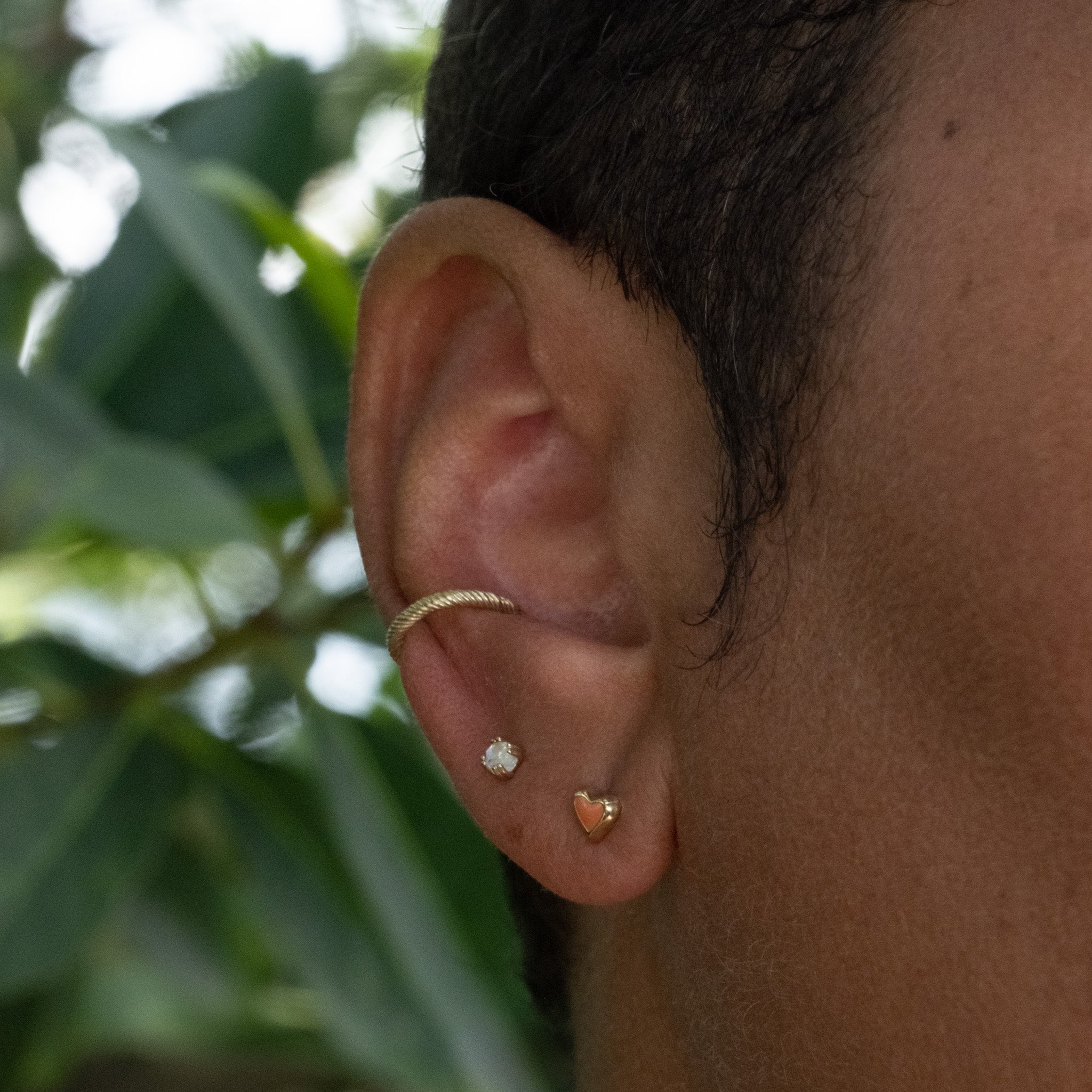 Solid gold tiny heart stud earring in coral enamel, rainbow moonstone stud, and twisted texture ear cuff, worn as ear stack.