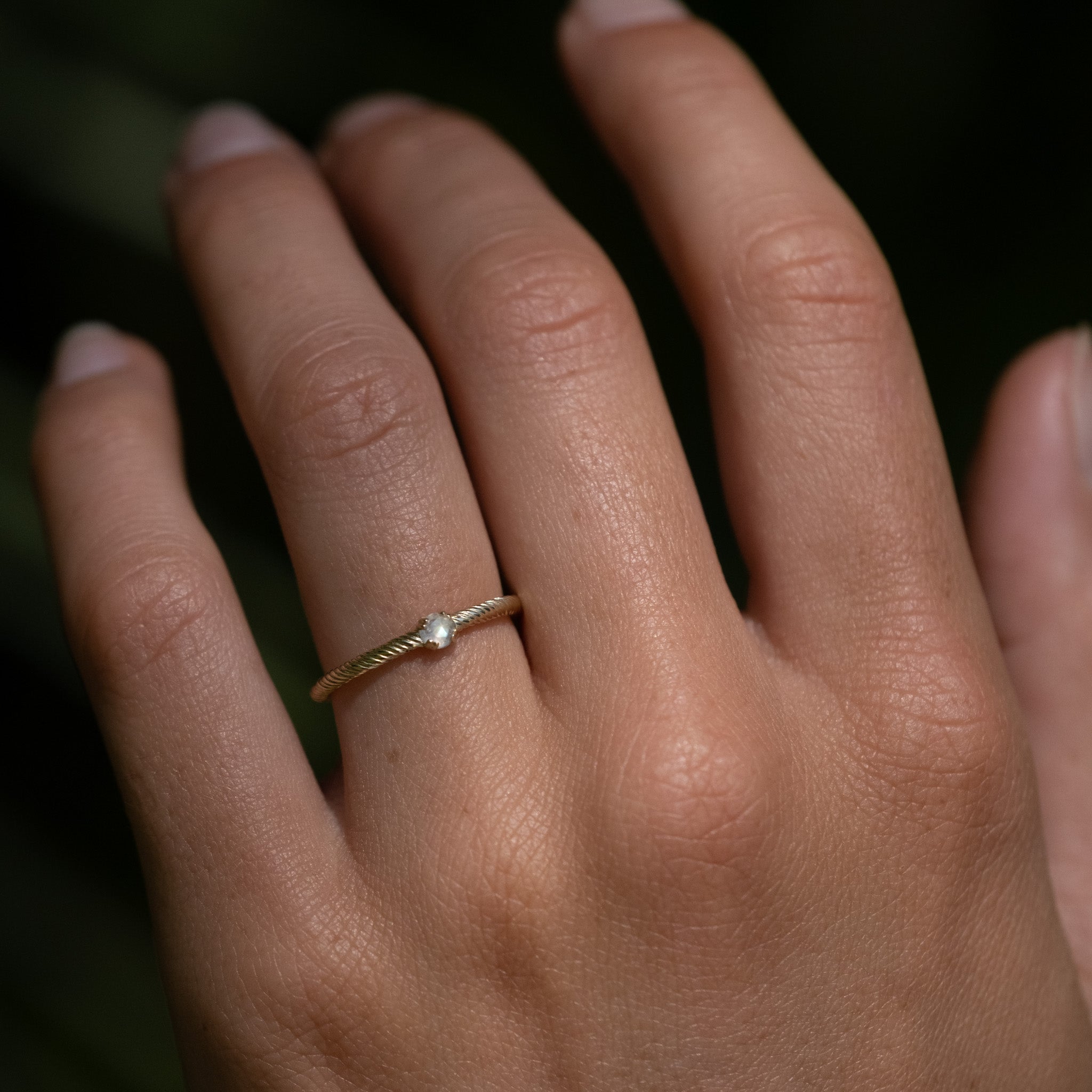 Minimalist solid gold stackable ring with twisted texture and solitaire rose cut faceted rainbow moonstone, worn on hand.