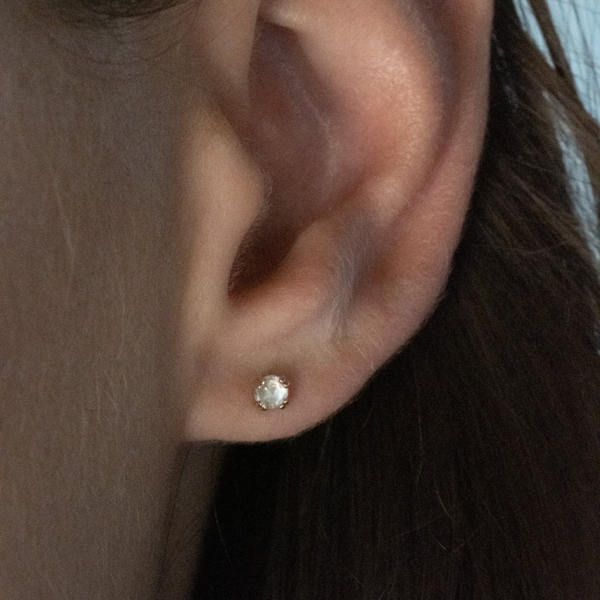 Small solid gold stud earring with rose cut faceted rainbow moonstone in a doubled prong setting, worn on ear.