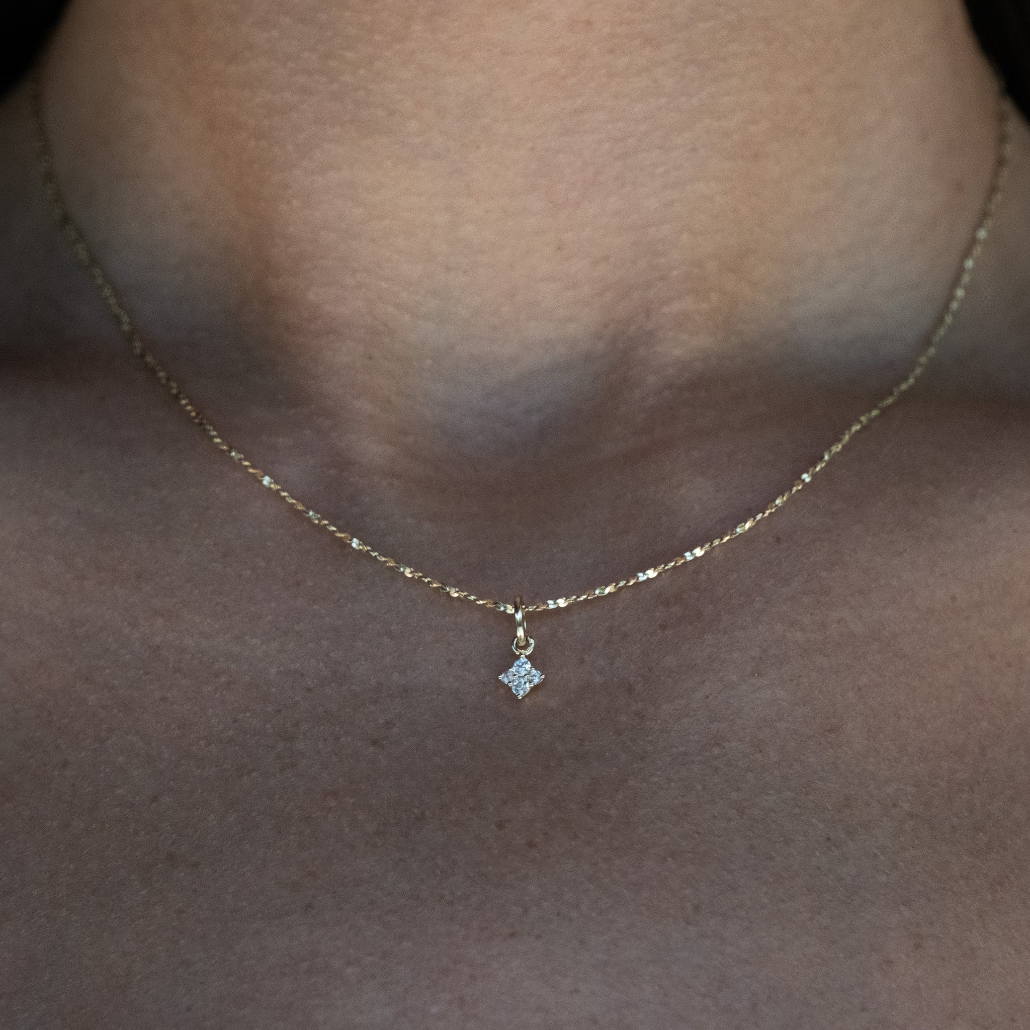 Solid gold tiny charm pendant with white sapphire, in a minimalist celestial design, hanging on chain, worn on neck.