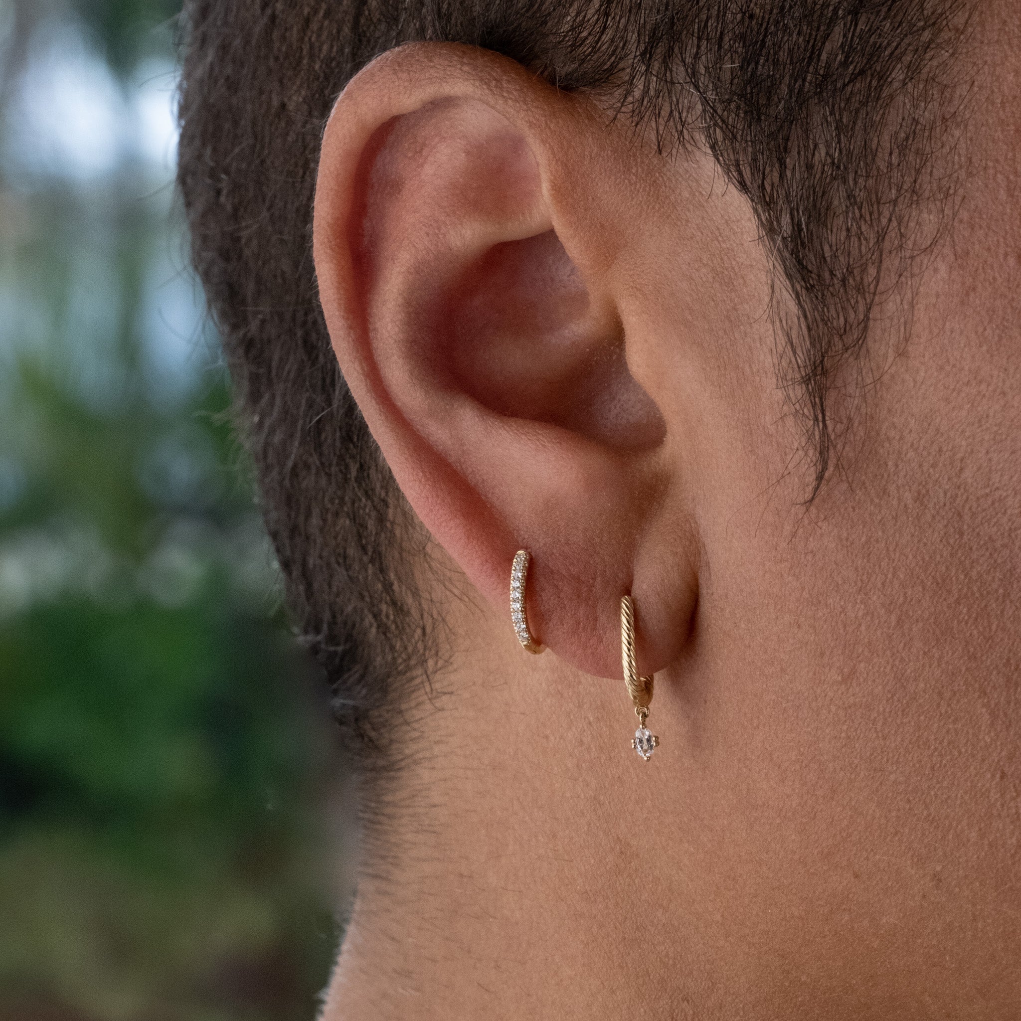 Solid gold diamond huggie hoop and huggie with twisted texture and oval white sapphire dangle shown in earring stack on ear.
