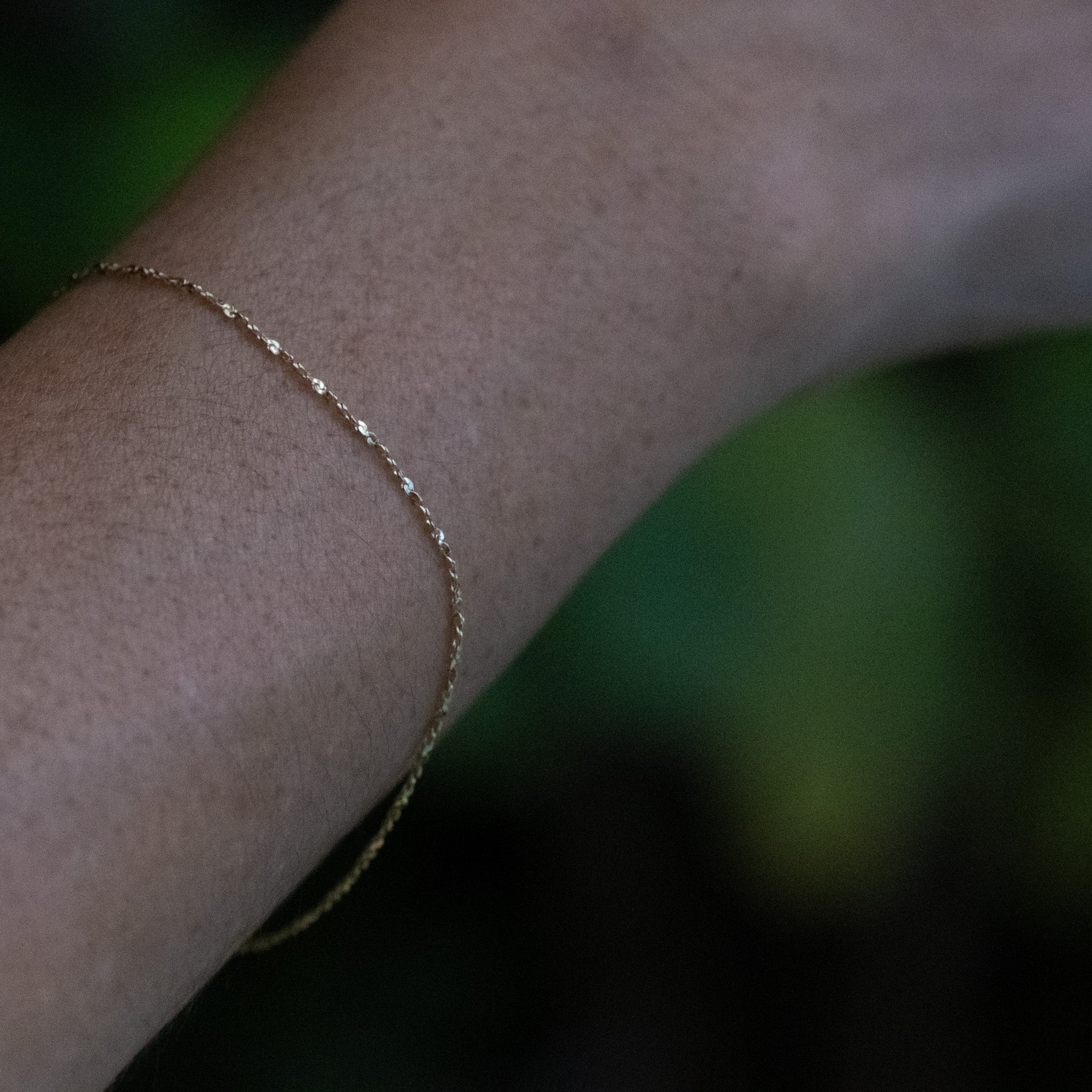 Delicate solid gold twisted serpentine chain bracelet with minimalist aesthetic, worn on wrist.