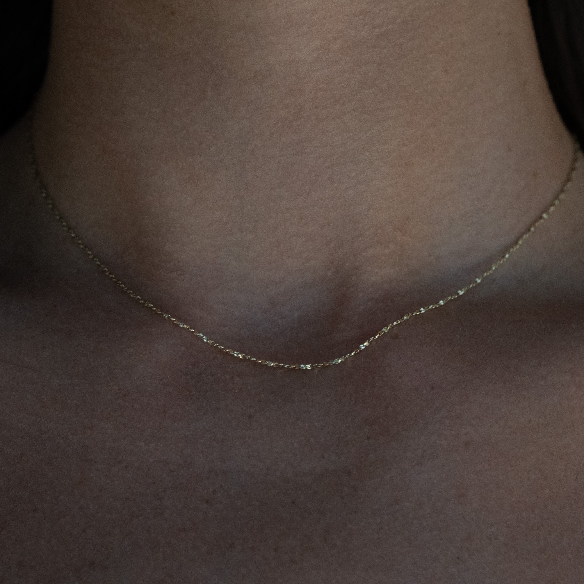 Delicate, sparkling solid gold twisted serpentine chain necklace with minimalist aesthetic, worn on neck.