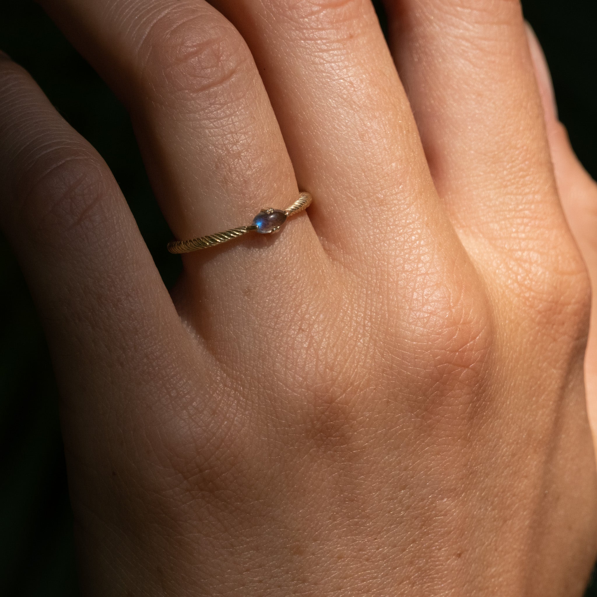 Solid gold solitaire ring with twisted texture, glowing oval cabochon labradorite, and minimalist design, worn on hand.