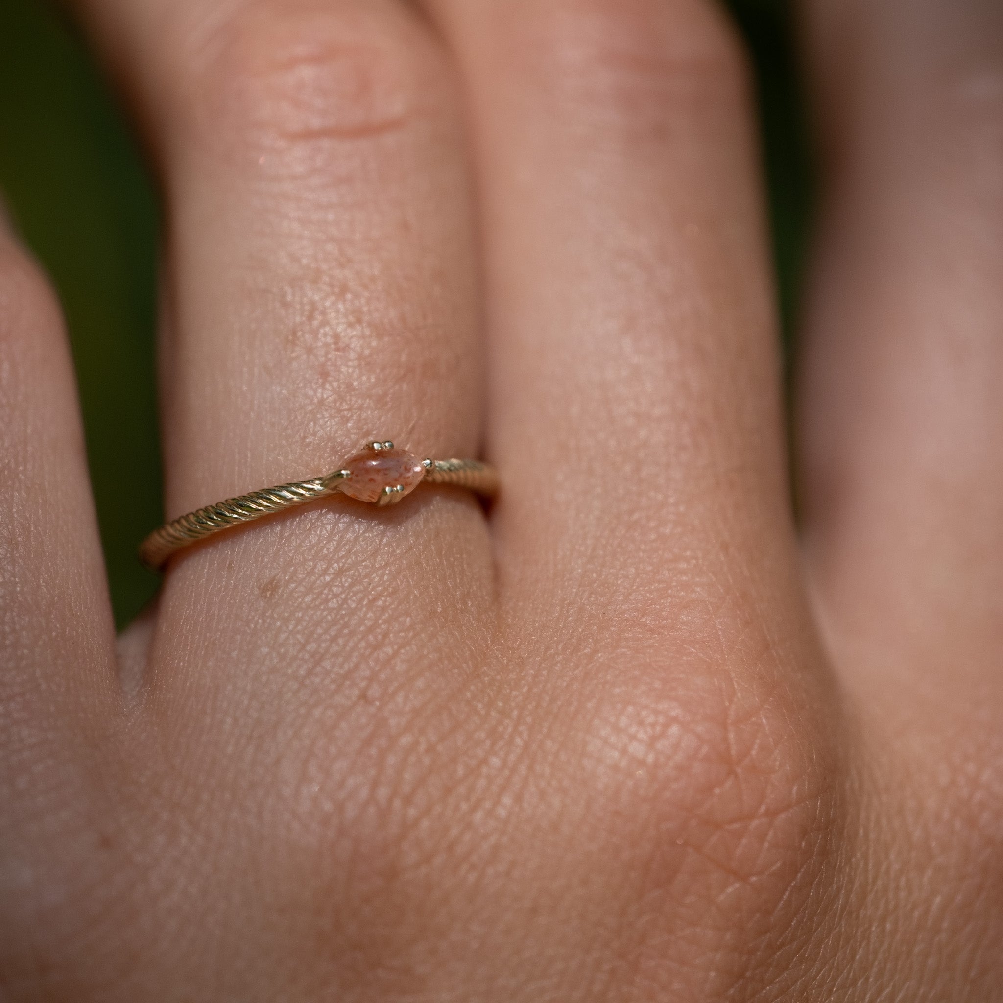 Close-up of solid gold solitaire ring with twisted texture and oval cabochon sunstone, worn on hand.