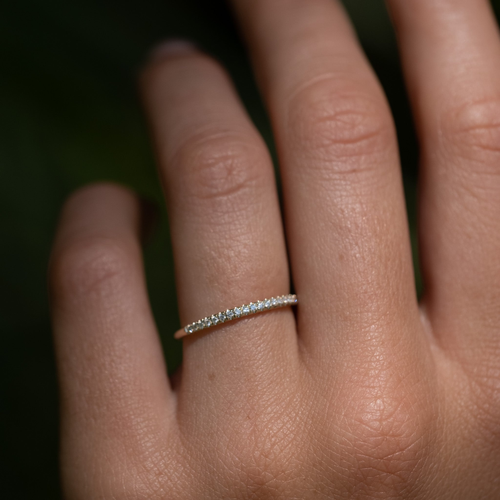 Close-up of thin solid gold stackable band ring with split-prong set brilliant diamonds, in a minimalist design, on hand.