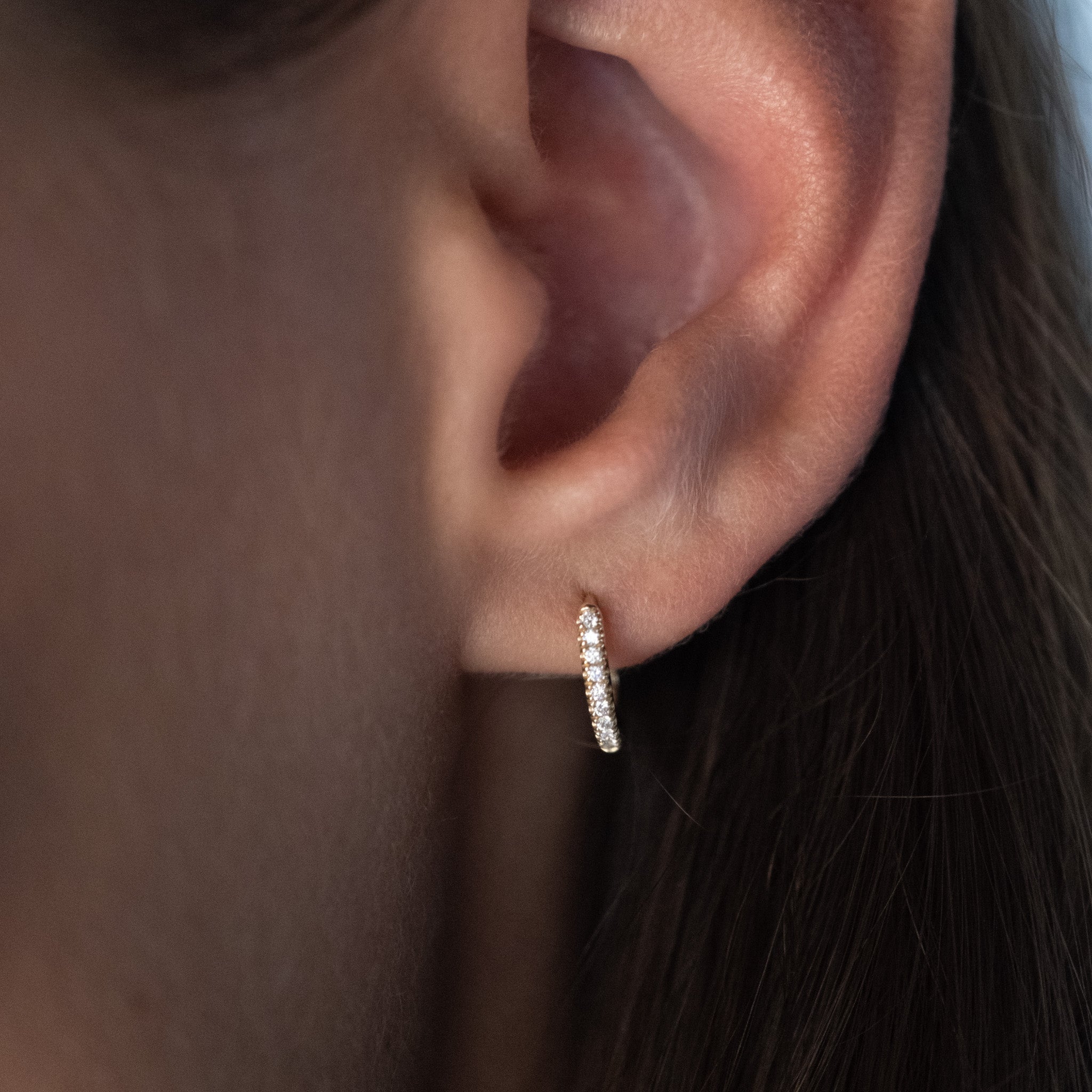 Solid gold huggie hoop earring with split-prong set brilliant white diamonds, in a minimalist design, worn on ear.