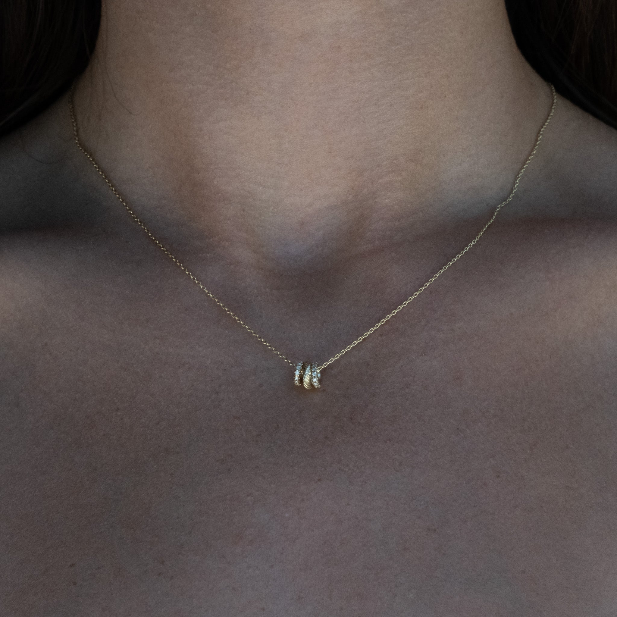 Solid gold necklace featuring textured and diamond oval link charms hanging on a cable chain, worn on neck.