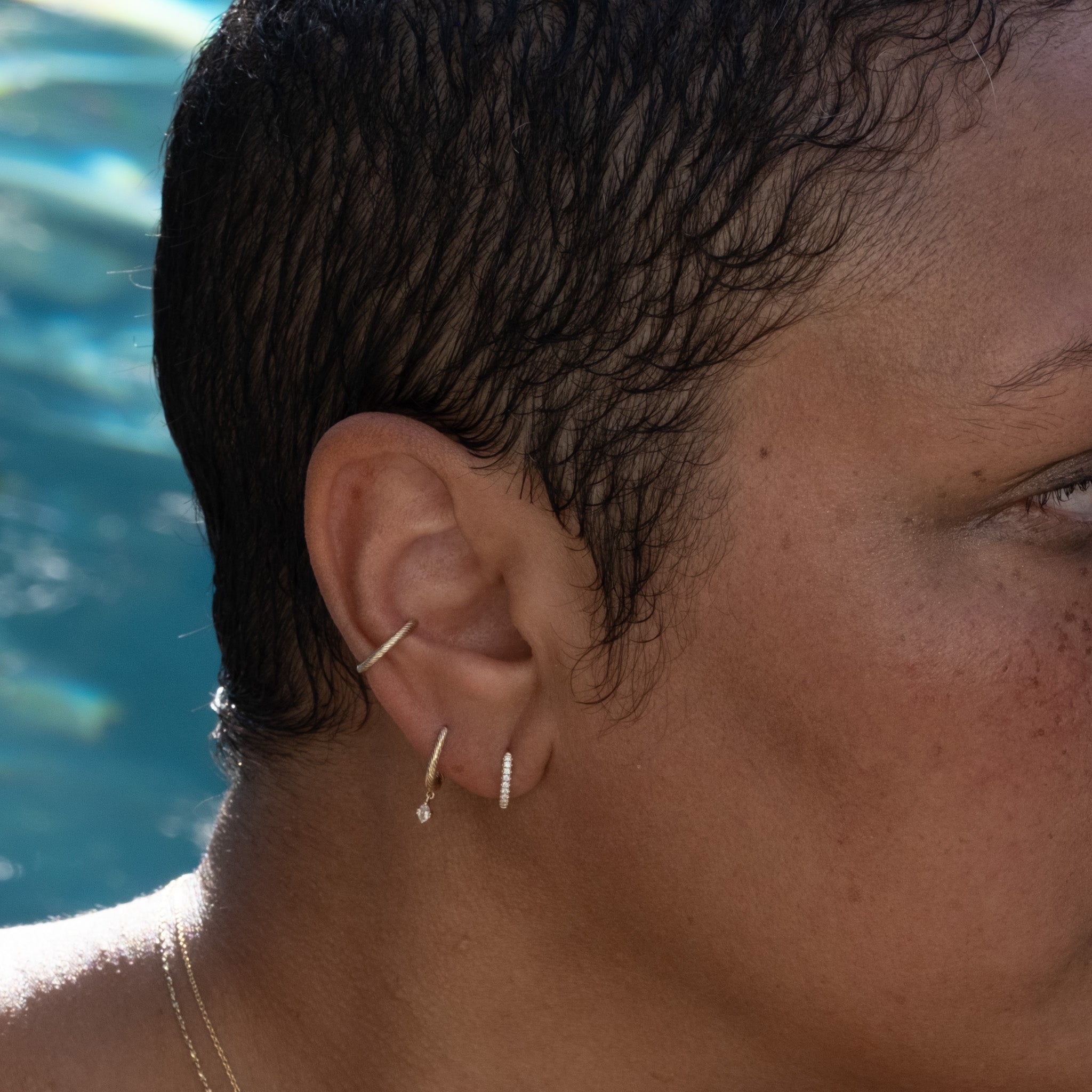 Solid gold huggie hoops earrings with diamonds and white sapphire drop, worn with cuff in twisted texture as ear stack.